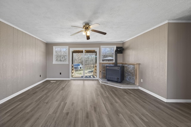 unfurnished living room with a healthy amount of sunlight, wood finished floors, a wood stove, and crown molding