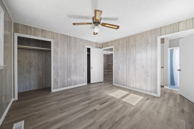 unfurnished bedroom featuring baseboards, wood finished floors, visible vents, and multiple closets