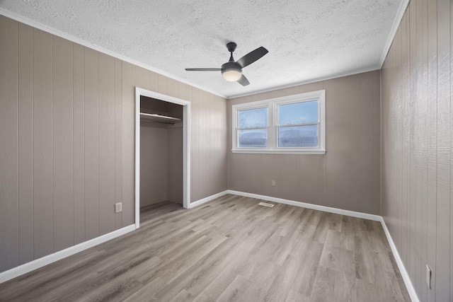 unfurnished bedroom with wood finished floors, baseboards, a closet, a textured ceiling, and crown molding