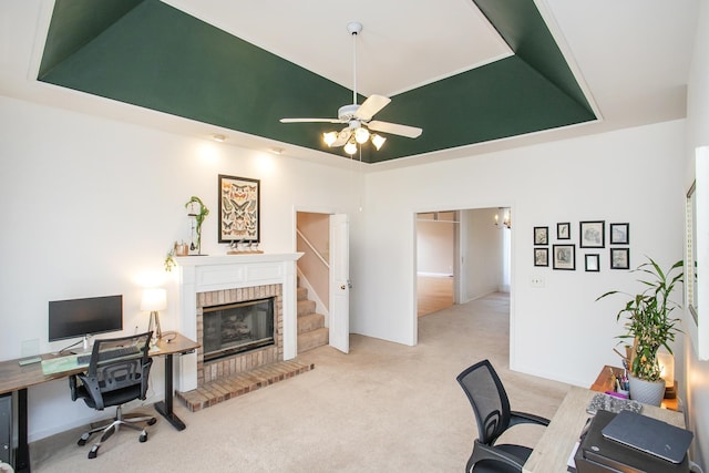 home office with a brick fireplace, a raised ceiling, ceiling fan, and carpet floors