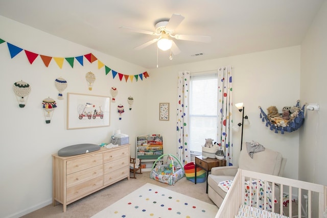 carpeted bedroom featuring visible vents, a nursery area, and a ceiling fan