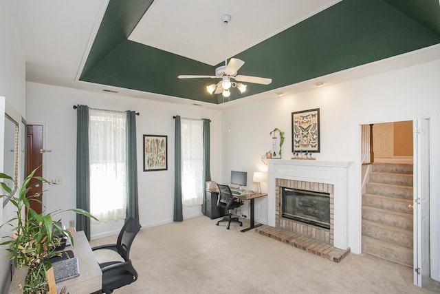 office with a ceiling fan, baseboards, a raised ceiling, a brick fireplace, and carpet flooring