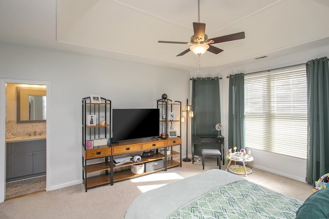 carpeted bedroom with a tray ceiling, baseboards, ensuite bathroom, and a sink