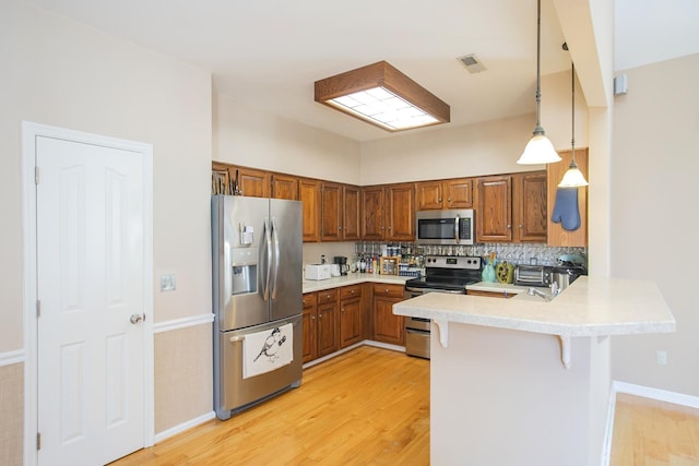 kitchen featuring light wood finished floors, a breakfast bar area, appliances with stainless steel finishes, a peninsula, and brown cabinetry