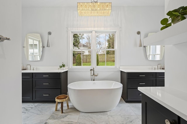 bathroom featuring a sink, a freestanding tub, two vanities, and marble finish floor