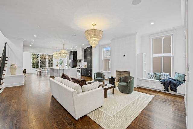 living area with dark wood finished floors, an inviting chandelier, stairway, and recessed lighting