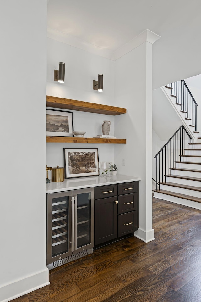 bar featuring beverage cooler, baseboards, a bar, dark wood-type flooring, and stairs