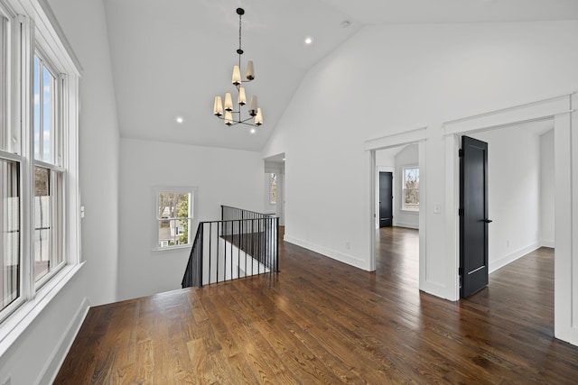 empty room featuring dark wood finished floors, high vaulted ceiling, plenty of natural light, and a chandelier