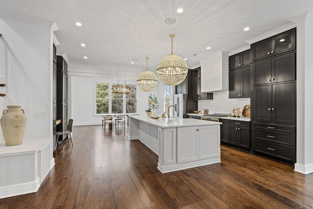 kitchen with dark wood finished floors, a kitchen island with sink, light countertops, decorative light fixtures, and backsplash