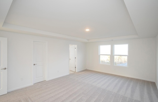 empty room featuring recessed lighting, a tray ceiling, baseboards, and light colored carpet