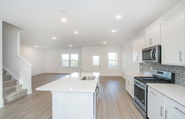 kitchen featuring a sink, backsplash, open floor plan, appliances with stainless steel finishes, and light countertops