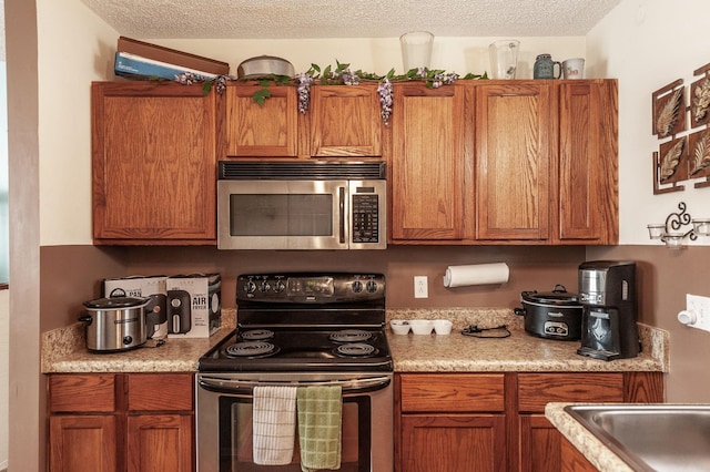 kitchen featuring stainless steel appliances, brown cabinets, a textured ceiling, and light countertops