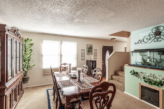 dining area featuring baseboards, stairway, light carpet, a glass covered fireplace, and a textured ceiling