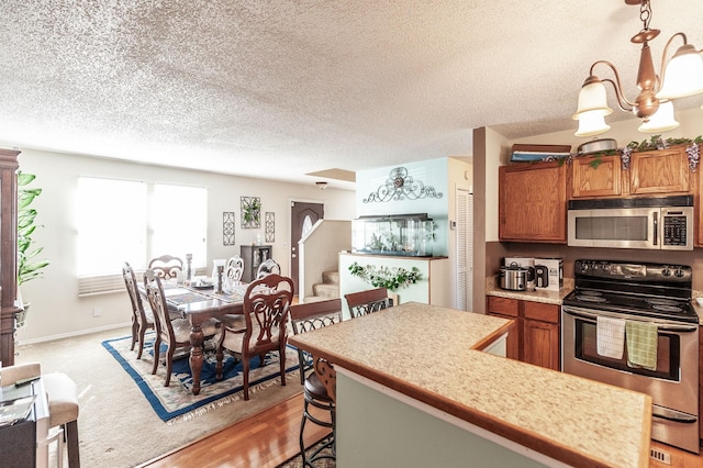 kitchen featuring appliances with stainless steel finishes, a breakfast bar area, brown cabinetry, light countertops, and a chandelier