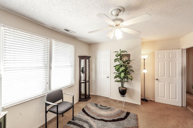 office space with visible vents, light colored carpet, a textured ceiling, and ceiling fan