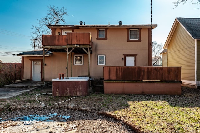 back of property featuring stucco siding, a hot tub, and a balcony