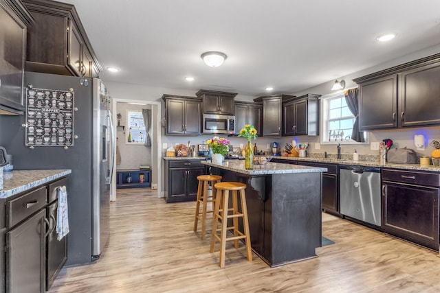 kitchen with a breakfast bar area, light stone counters, stainless steel appliances, dark brown cabinetry, and light wood-type flooring