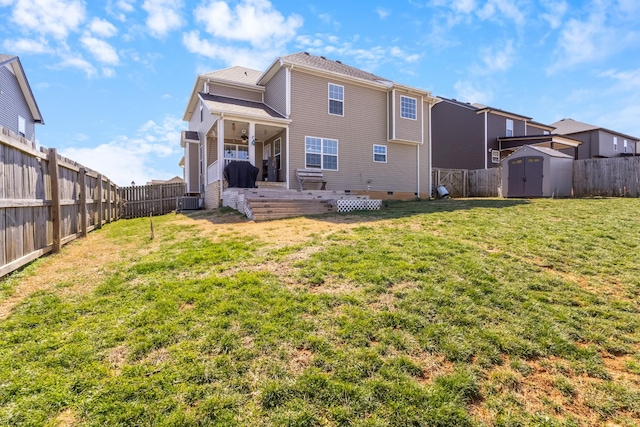 back of house featuring an outbuilding, a fenced backyard, a storage unit, crawl space, and a lawn