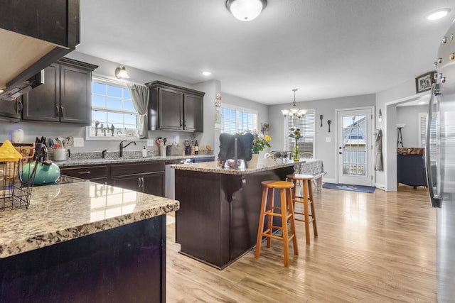 kitchen with a healthy amount of sunlight, a sink, a kitchen bar, light wood-type flooring, and a center island