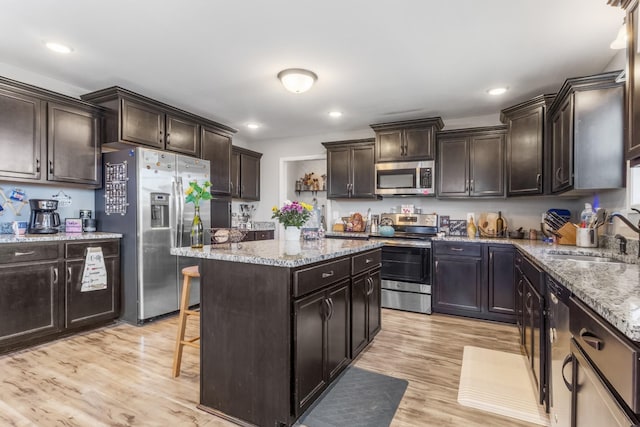 kitchen with a kitchen island, a sink, dark brown cabinetry, light wood-style floors, and appliances with stainless steel finishes