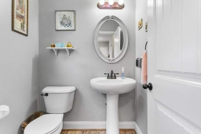 half bathroom featuring toilet, wood finished floors, baseboards, and a sink