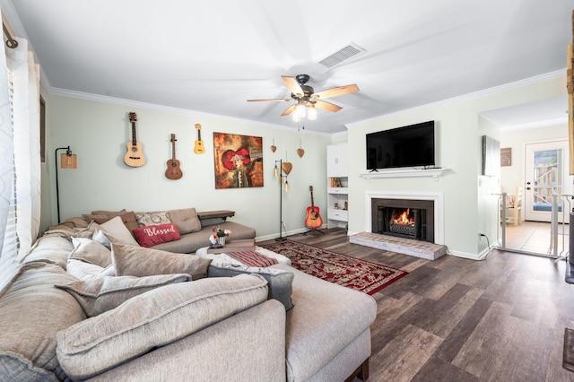 living room with a ceiling fan, wood finished floors, visible vents, a warm lit fireplace, and ornamental molding