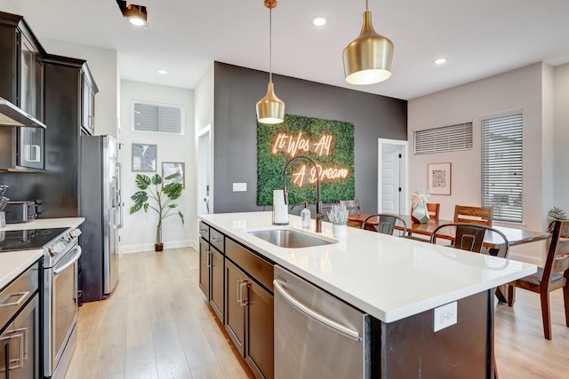 kitchen featuring light wood-type flooring, a kitchen island with sink, a sink, appliances with stainless steel finishes, and light countertops