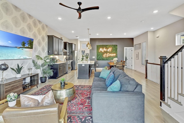 living area with stairway, baseboards, light wood finished floors, recessed lighting, and ceiling fan