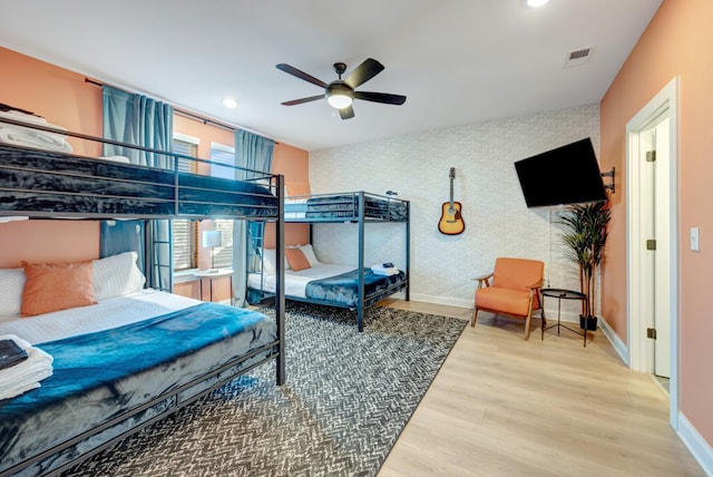 bedroom featuring wood finished floors, visible vents, baseboards, wallpapered walls, and an accent wall