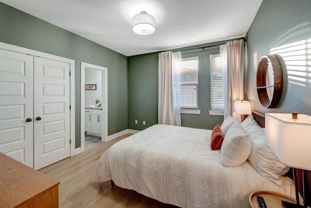 bedroom with a closet, ensuite bath, baseboards, and wood finished floors