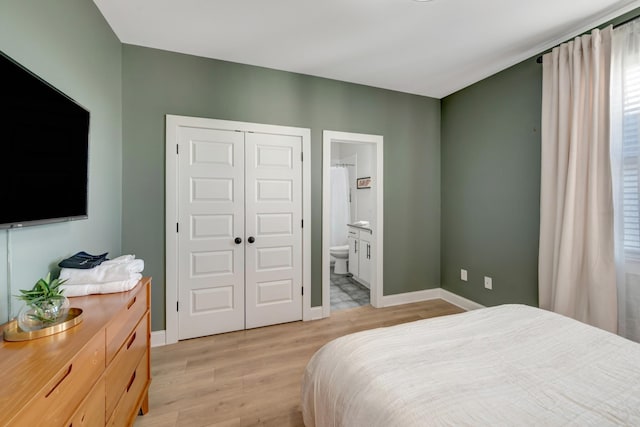 bedroom with a closet, light wood-style flooring, ensuite bath, and baseboards