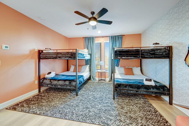 bedroom featuring wallpapered walls, a ceiling fan, baseboards, and wood finished floors