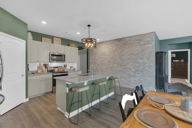 kitchen with a sink, wood finished floors, appliances with stainless steel finishes, and a breakfast bar area