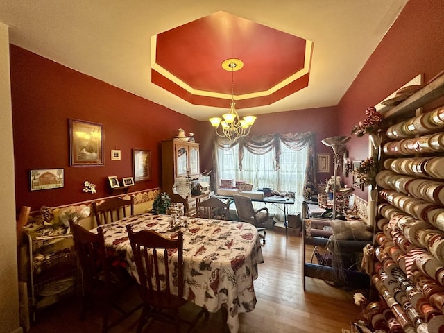 dining area with a notable chandelier, a raised ceiling, and wood-type flooring