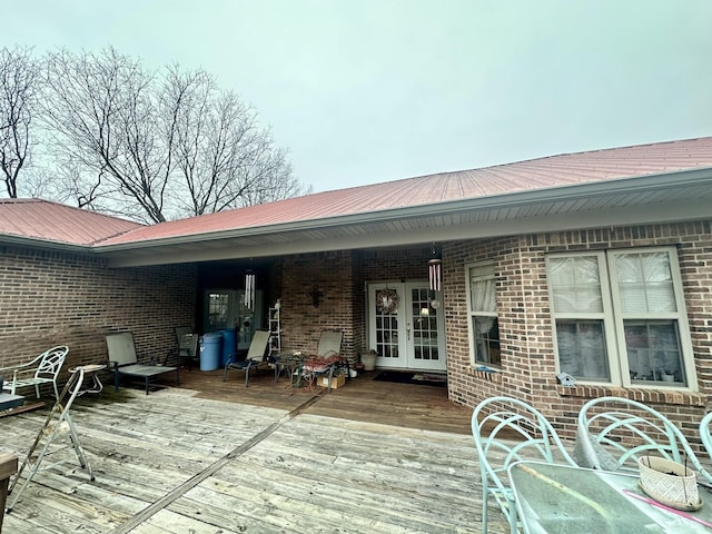 exterior space with a wooden deck, french doors, brick siding, and metal roof