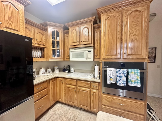 kitchen with glass insert cabinets, white appliances, light countertops, and light tile patterned flooring