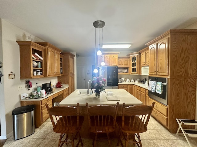 kitchen with a sink, decorative light fixtures, appliances with stainless steel finishes, light countertops, and glass insert cabinets