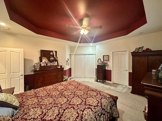 tiled bedroom with a ceiling fan, a tray ceiling, and carpet floors