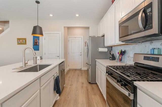 kitchen with a sink, tasteful backsplash, white cabinetry, stainless steel appliances, and light countertops