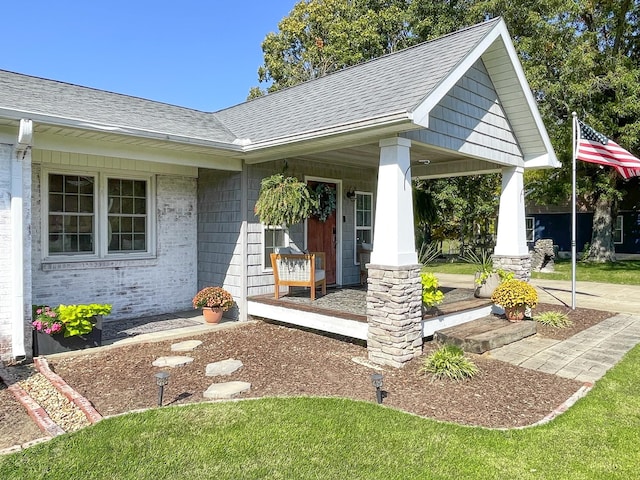 view of exterior entry featuring brick siding, a porch, and a shingled roof