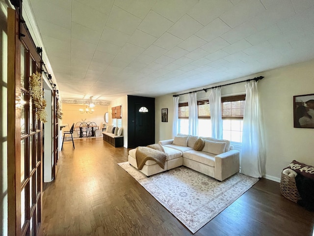 living room featuring an inviting chandelier, a barn door, wood finished floors, and baseboards