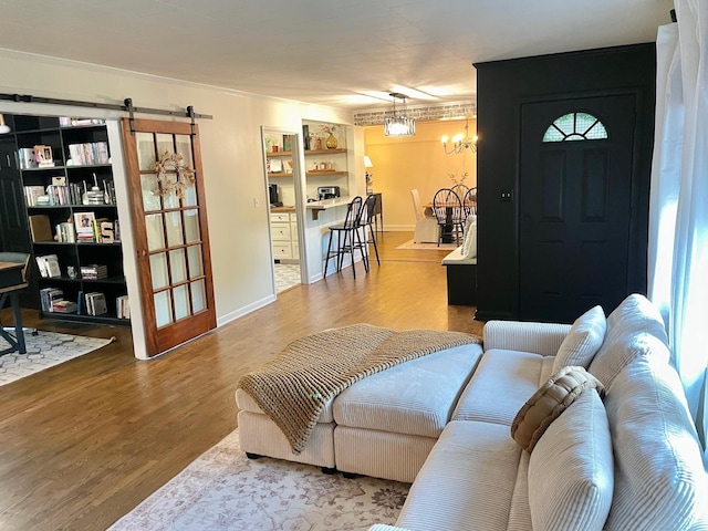 living area featuring an inviting chandelier, baseboards, a barn door, and wood finished floors