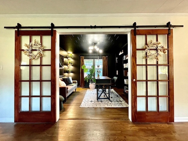 doorway to outside featuring a barn door, wood finished floors, baseboards, and ornamental molding