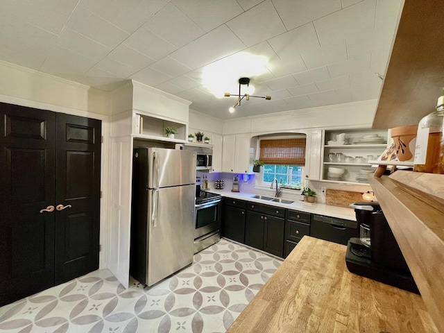 kitchen with dark cabinetry, open shelves, a sink, light countertops, and appliances with stainless steel finishes