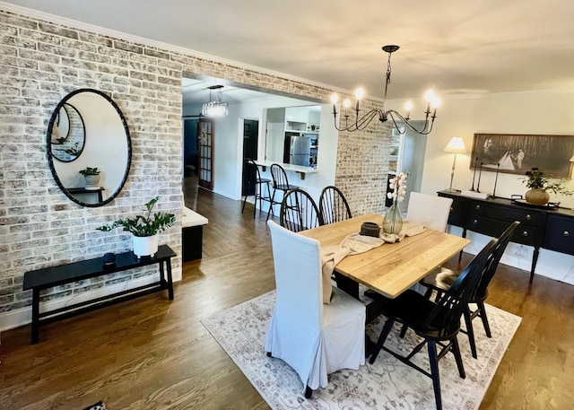 dining room featuring an inviting chandelier, wood finished floors, baseboards, and brick wall