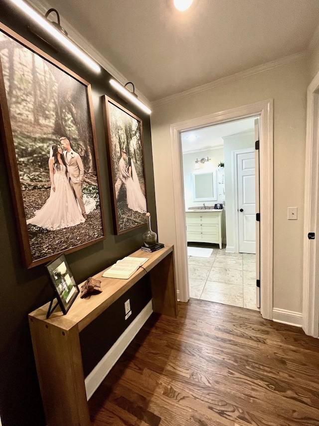 hallway with a sink, wood finished floors, baseboards, and ornamental molding