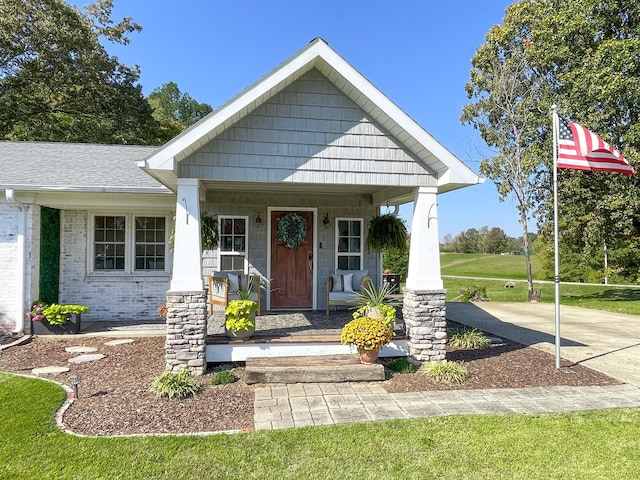 view of front of property with brick siding, a porch, a front lawn, and a shingled roof