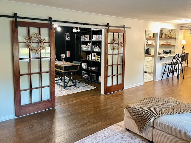 living area with a barn door, baseboards, wood finished floors, and crown molding