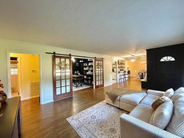 living room with built in shelves, wood finished floors, visible vents, baseboards, and a barn door