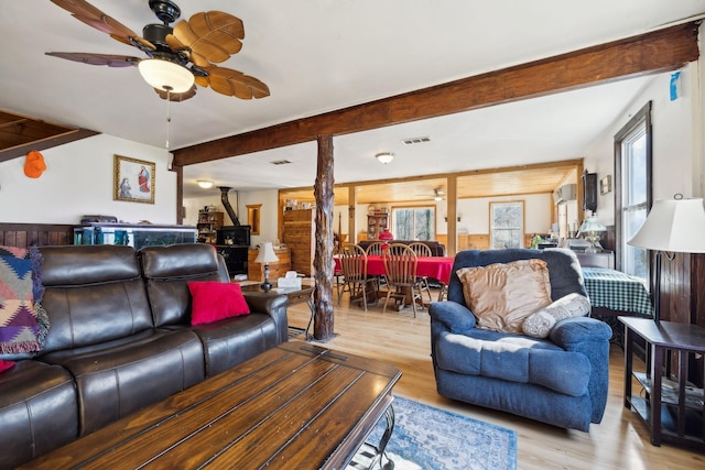 living room with visible vents, light wood-style floors, beamed ceiling, and ceiling fan